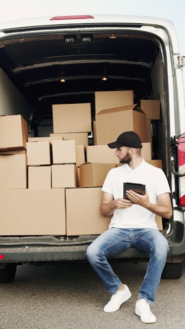 Black-coated man wearing a cap is in the process of opening the driver's side door of a white van, which is parked on a paved street. The van's front window and side mirror are visible, along with the